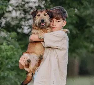 un chien est tenu dans les bras de son jeune maitre