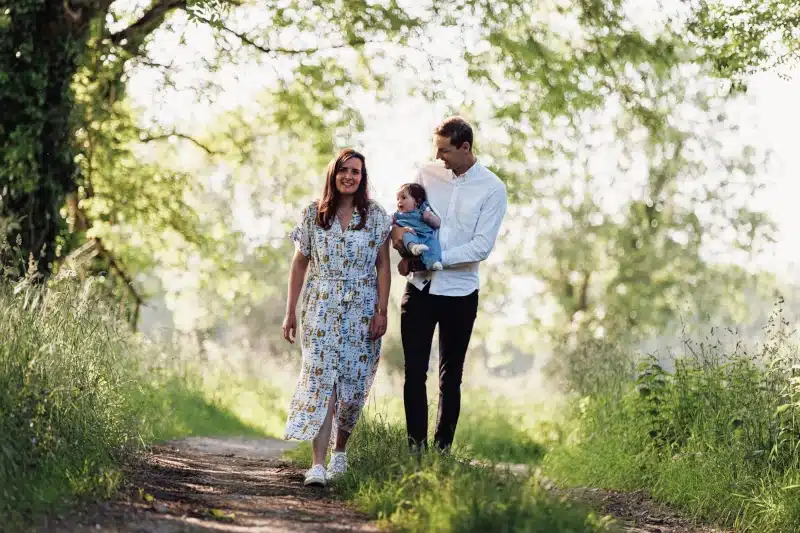 couple avec un bébé dans les bras marchant sur un chemin forestier