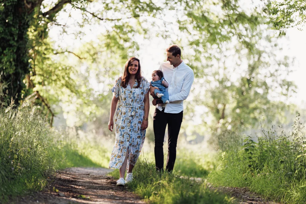couple avec un bébé dans les bras marchant sur un chemin forestier